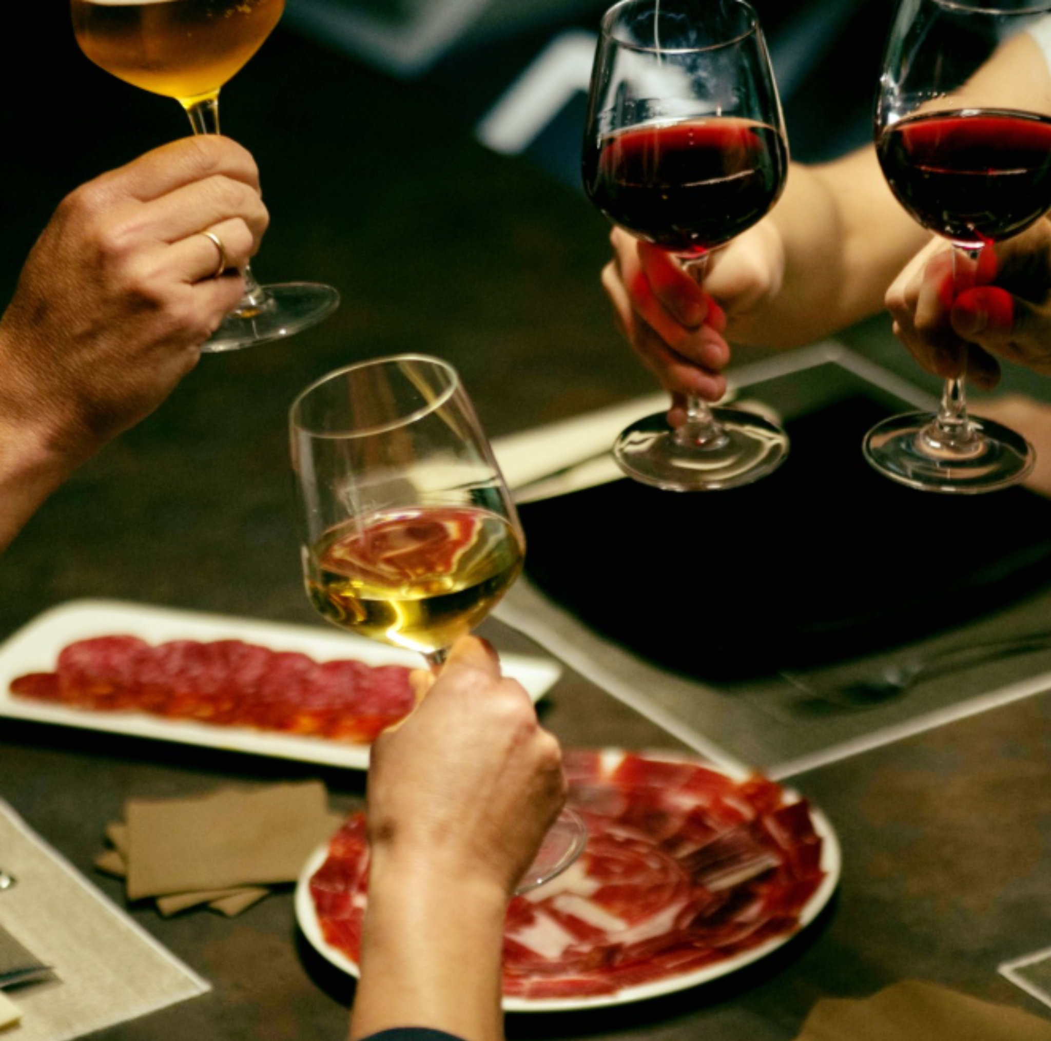 People holding wine glasses with different types of wine around a table with plates of food.