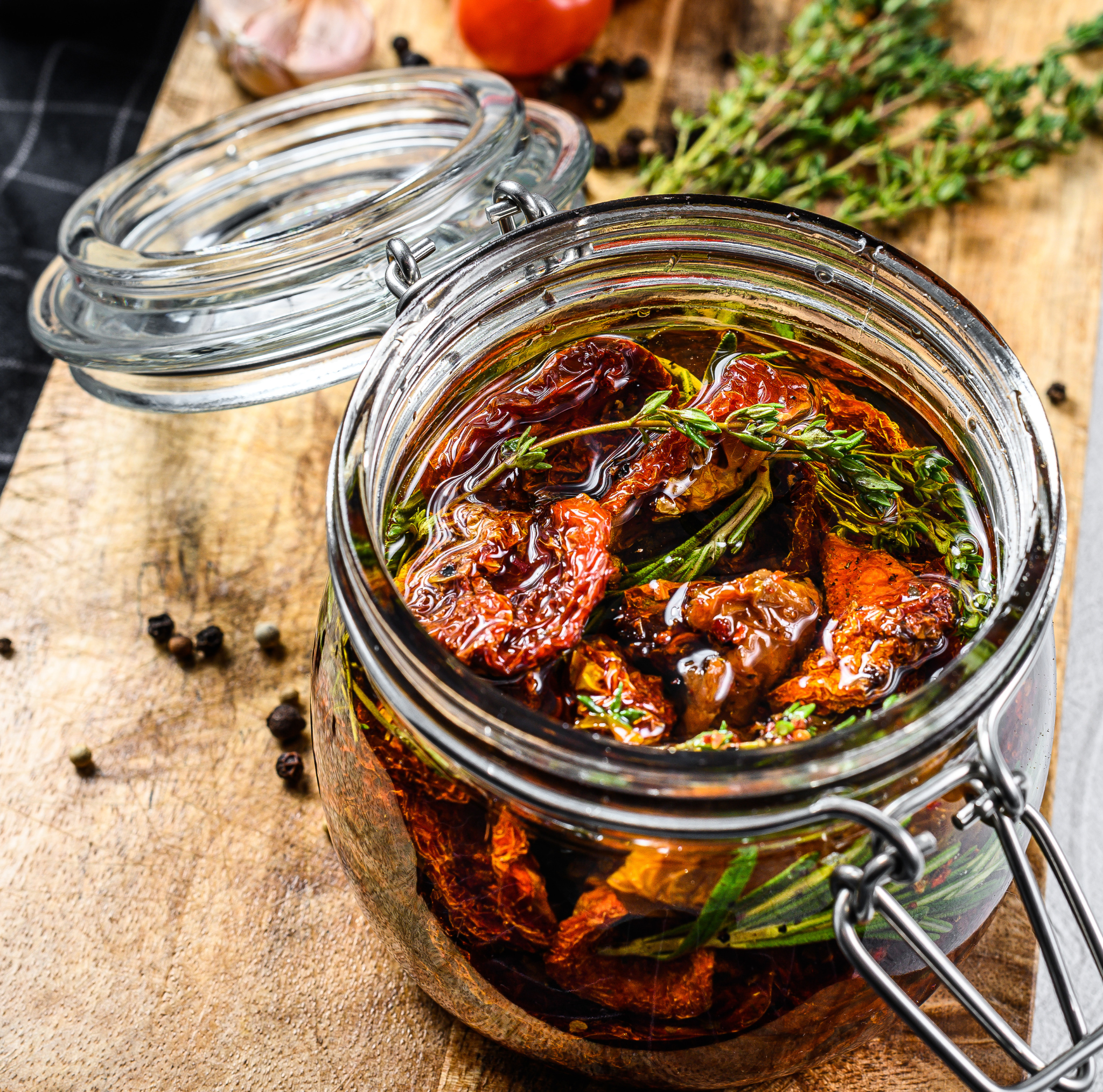 Glass jar with sun-dried tomatoes and herbs on a wooden surface