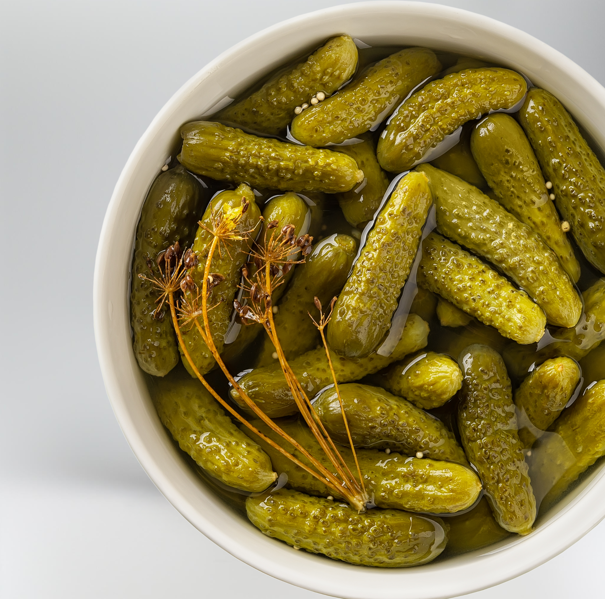 White bowl filled with pickles on a light gray background
