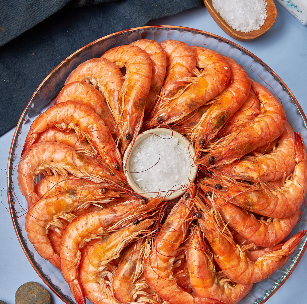 Platter of cooked shrimp with a small bowl of salt on a blue surface