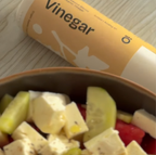 Salad with a container of white balsamic vinegar on a wooden surface