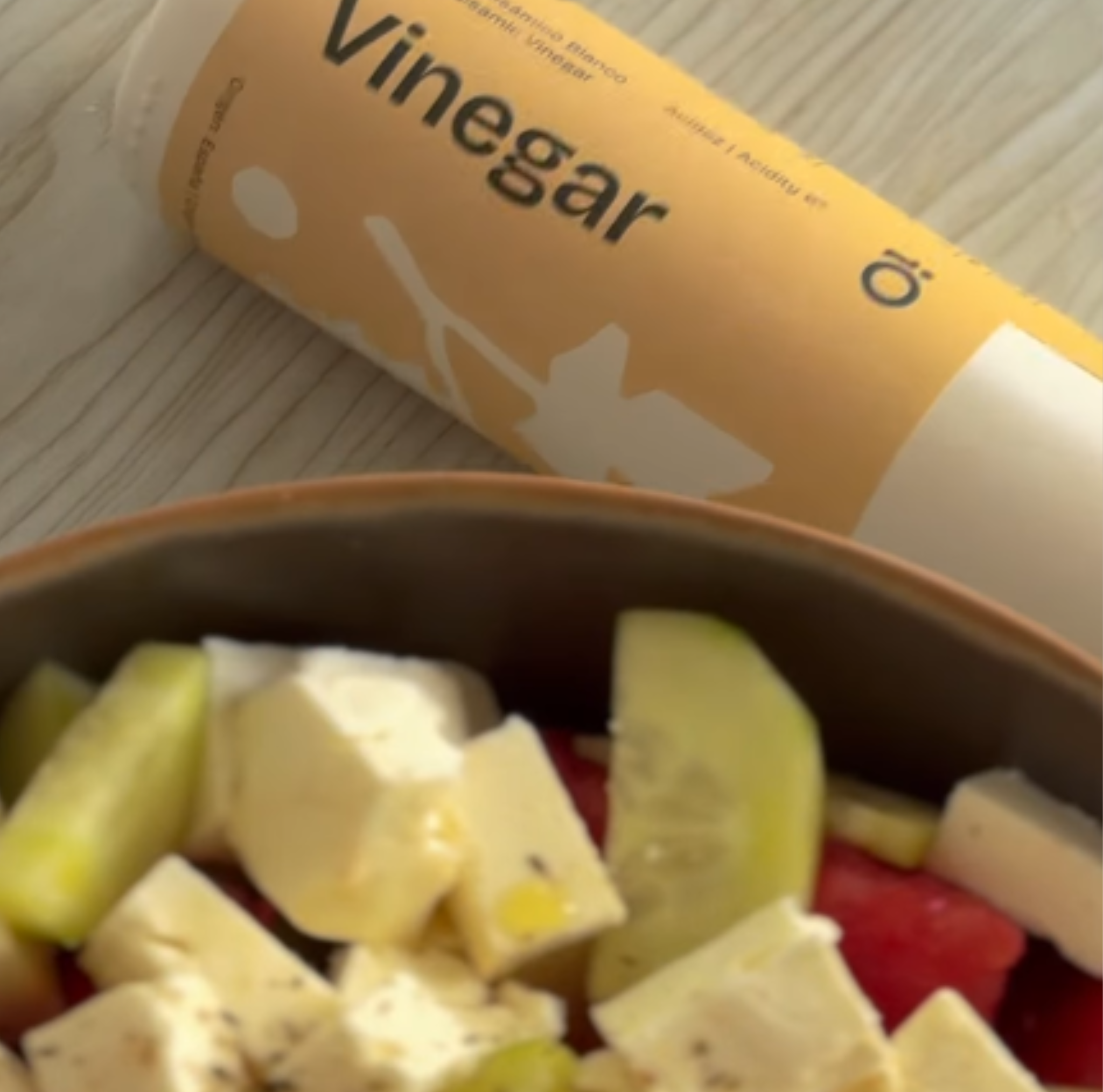 Salad with a container of white balsamic vinegar on a wooden surface